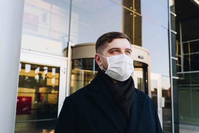 Man, young professional, outside his office during coronavirus COVID-19 outbreak and pandemic wearing a face mask