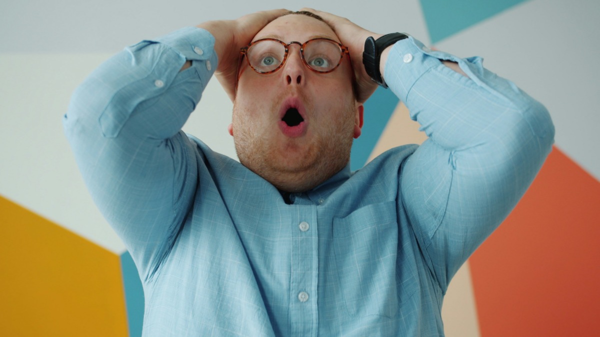 Angry guy in glasses is yelling holding head gesturing looking at camera on colorful background. Negative emotions, feelings and modern people concept.