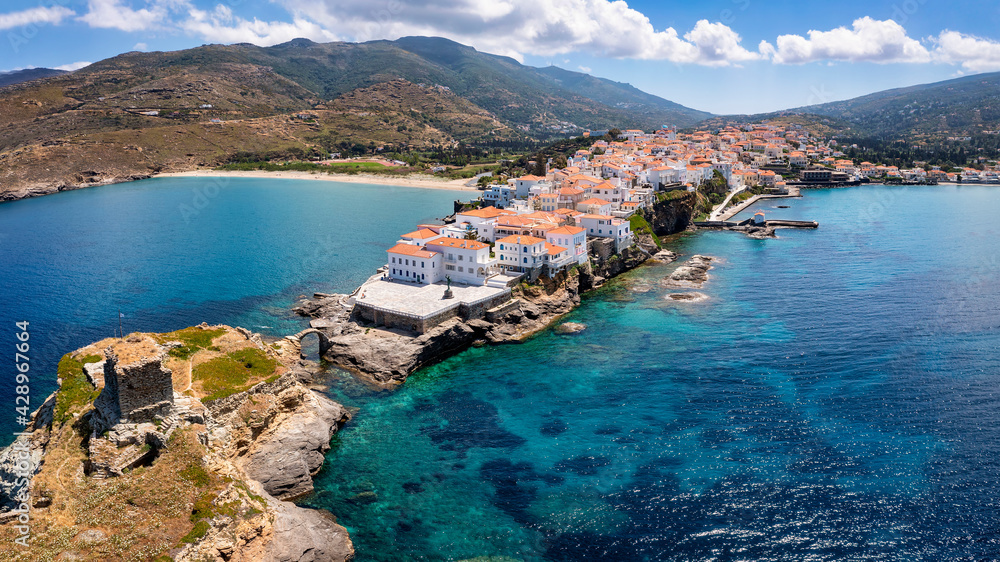 Aerial view to the idyllic town of Andros island, with the fortress by the turquoise sea, Cyclades, Greece